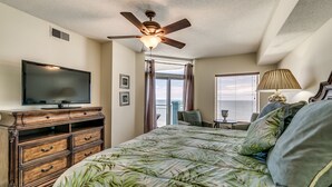 Ein Schlafzimmer mit Bett, Fernseher, Deckenventilator, Fenster mit Vorhängen und einer Lampe.