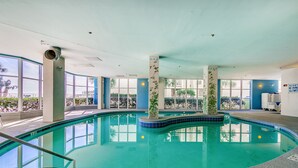 Ein Hallenbad mit klarem, blauen Wasser, umgeben von großen Fenstern und Säulen.