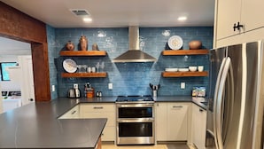 Una cocina moderna con una isla central, horno empotrado, refrigerador de acero inoxidable y salpicadero de azulejos azules.