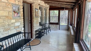 Un espacio al aire libre techado, con paredes de piedra, bancos de madera y suelo de hormigón.