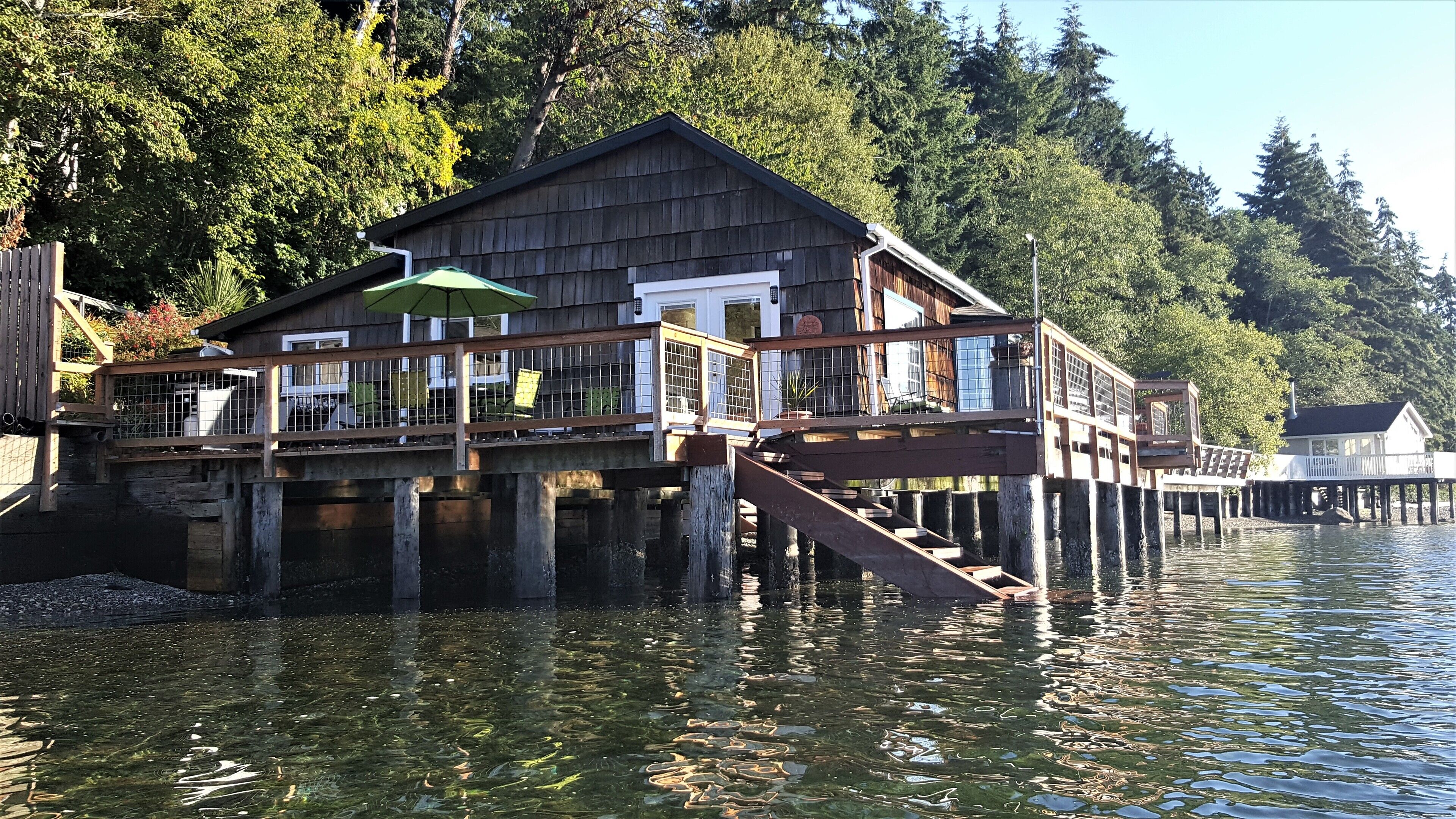 Une cabane en bois dotée d’une terrasse qui s’étend au-dessus de l’eau, entourée d’arbres.