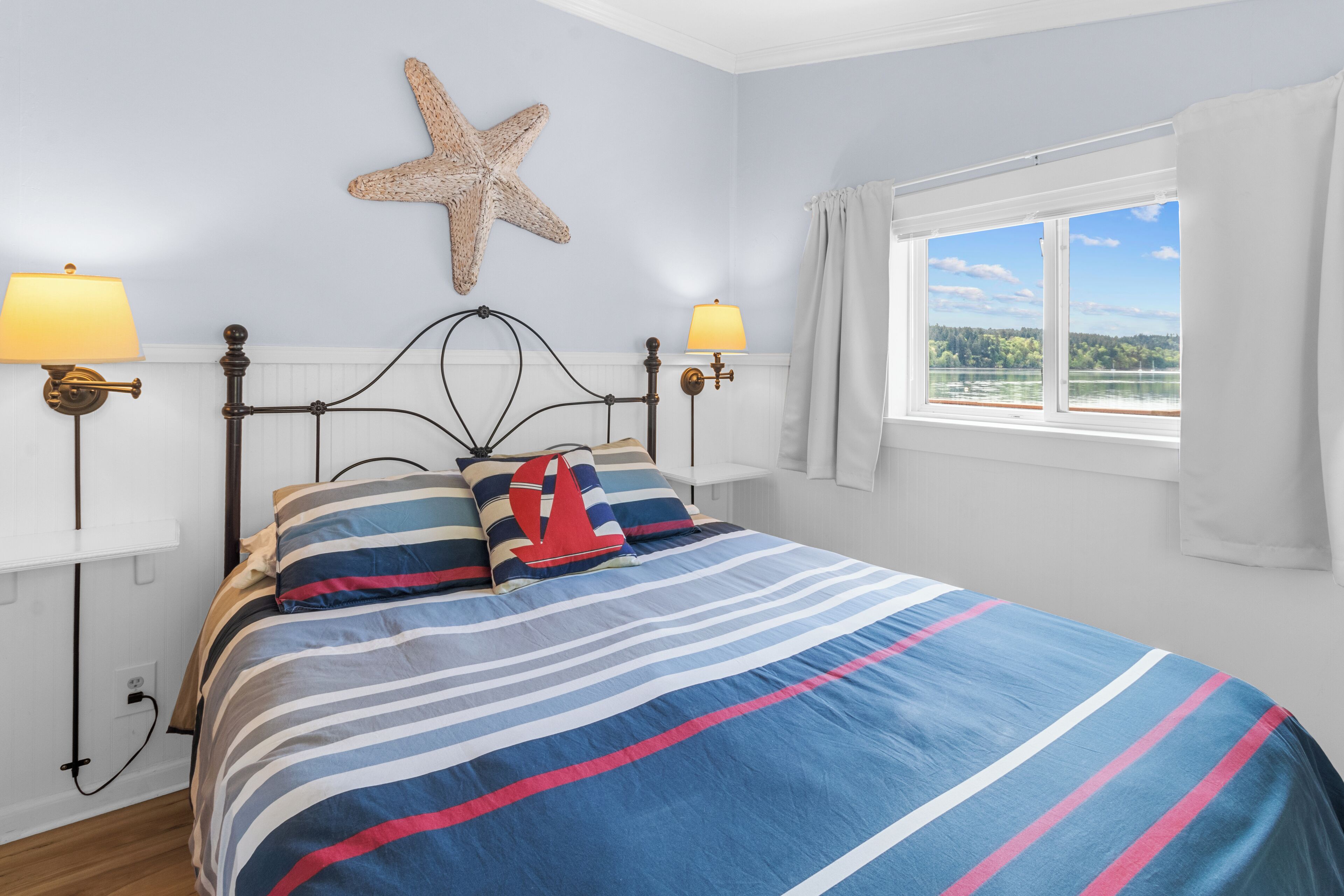 A bed with striped bedding, a starfish decoration on the wall, and a window with a view of a body of water.