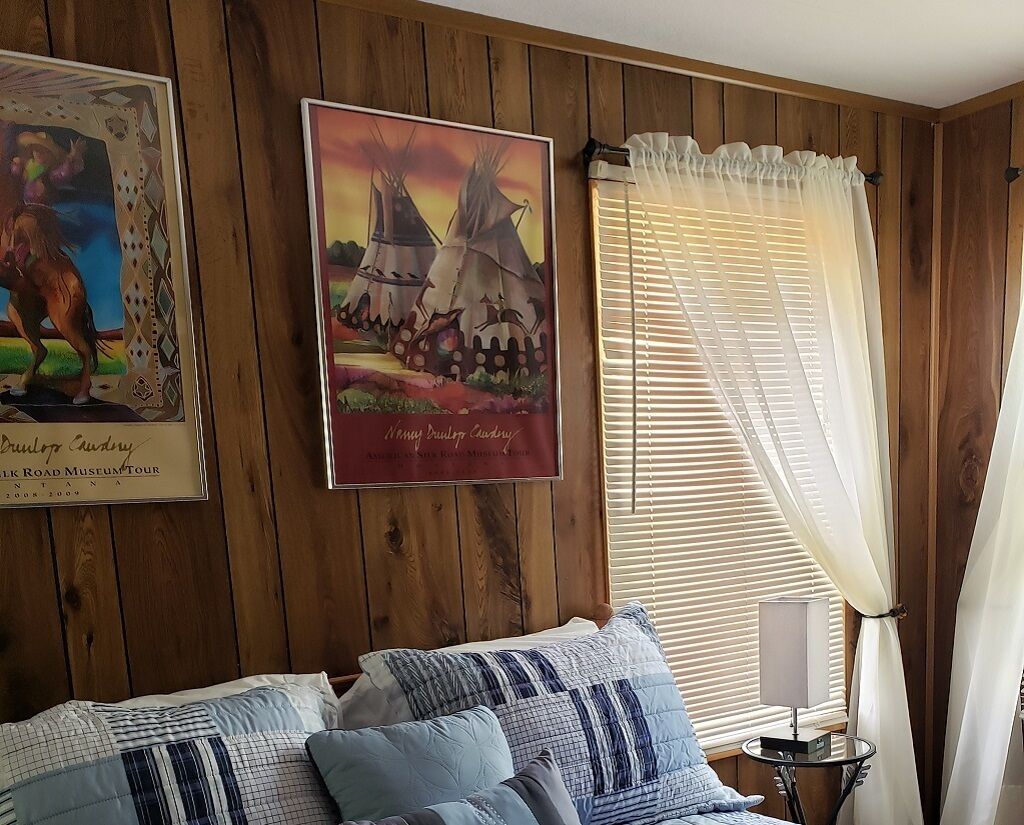 Una habitación con paneles de madera, una cama con ropa de cama estampada, un cuadro enmarcado de un caballo y una ventana con persianas.