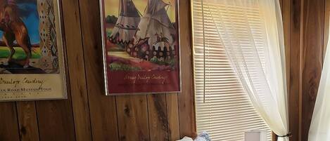 Una habitación con paneles de madera, una cama con ropa de cama estampada, un cuadro enmarcado de un caballo y una ventana con persianas.