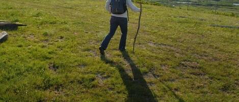 A person hiking on a grassy field with a backpack and walking stick.