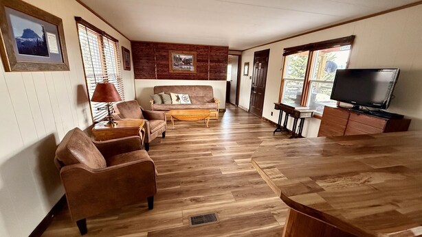 Een ruime woonkamer met een bank, fauteuils, een salontafel, een televisie en houten vloeren.