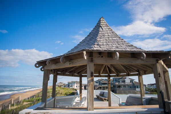 A wooden gazebo with a sloped roof overlooking a beach.