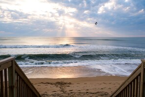A beach with wooden railings, waves, and a bird flying.