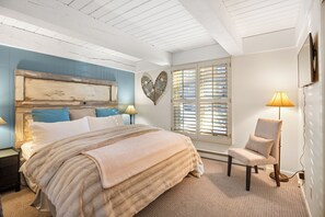 A bedroom with a large bed, a chair, a heart-shaped wall decoration, and a window with blinds. - Aspen Mountain Views, Bright Corner 2BR, Pool, Hot Tub, 7-Min Walk to Gondola (Aspen)