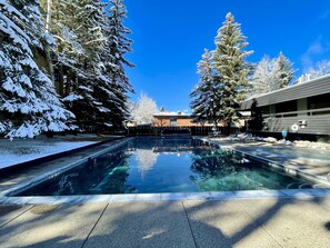 A clear pool surrounded by snow-covered trees, with a building in the background. - Aspen Mountain Views, Bright Corner 2BR, Pool, Hot Tub, 7-Min Walk to Gondola (Aspen)