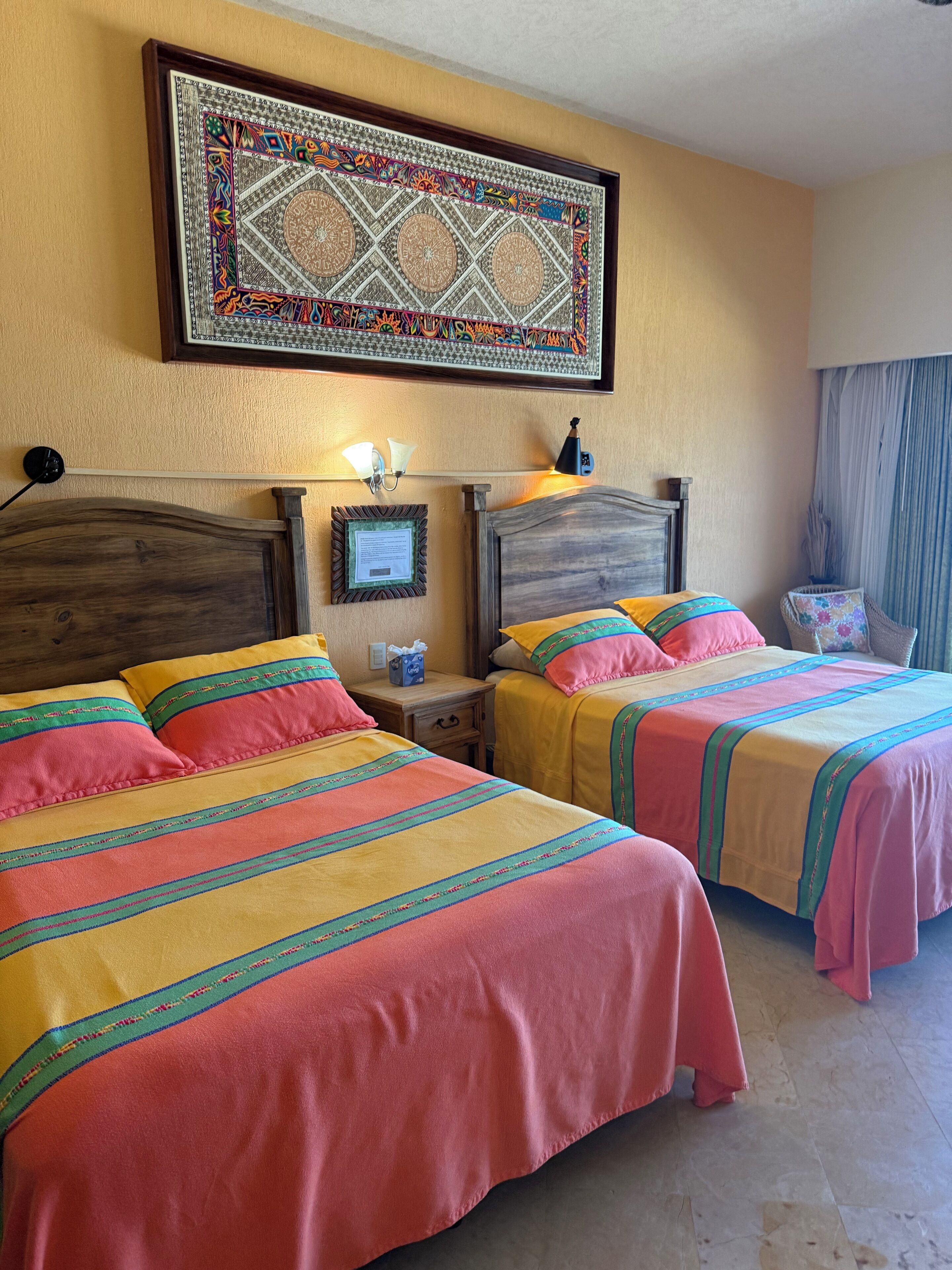 A hotel room with two beds, a wall hanging, a nightstand, and a lamp.