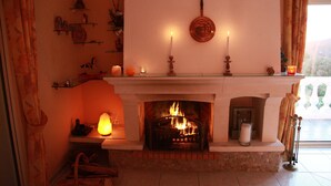 A fireplace with a fire, a mantel with candles, and a view of the outdoors through a window.