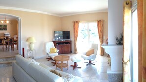 A living room with a sofa, armchairs, a coffee table, a TV, and a dining area with chairs and a table.