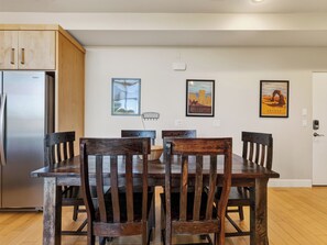 A dining area with a wooden table and chairs, a refrigerator, and wall-mounted artwork.