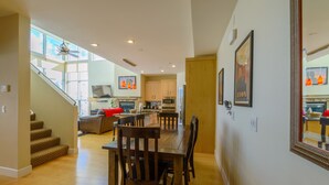A spacious living area with a dining table, chairs, and a staircase leading to a balcony.