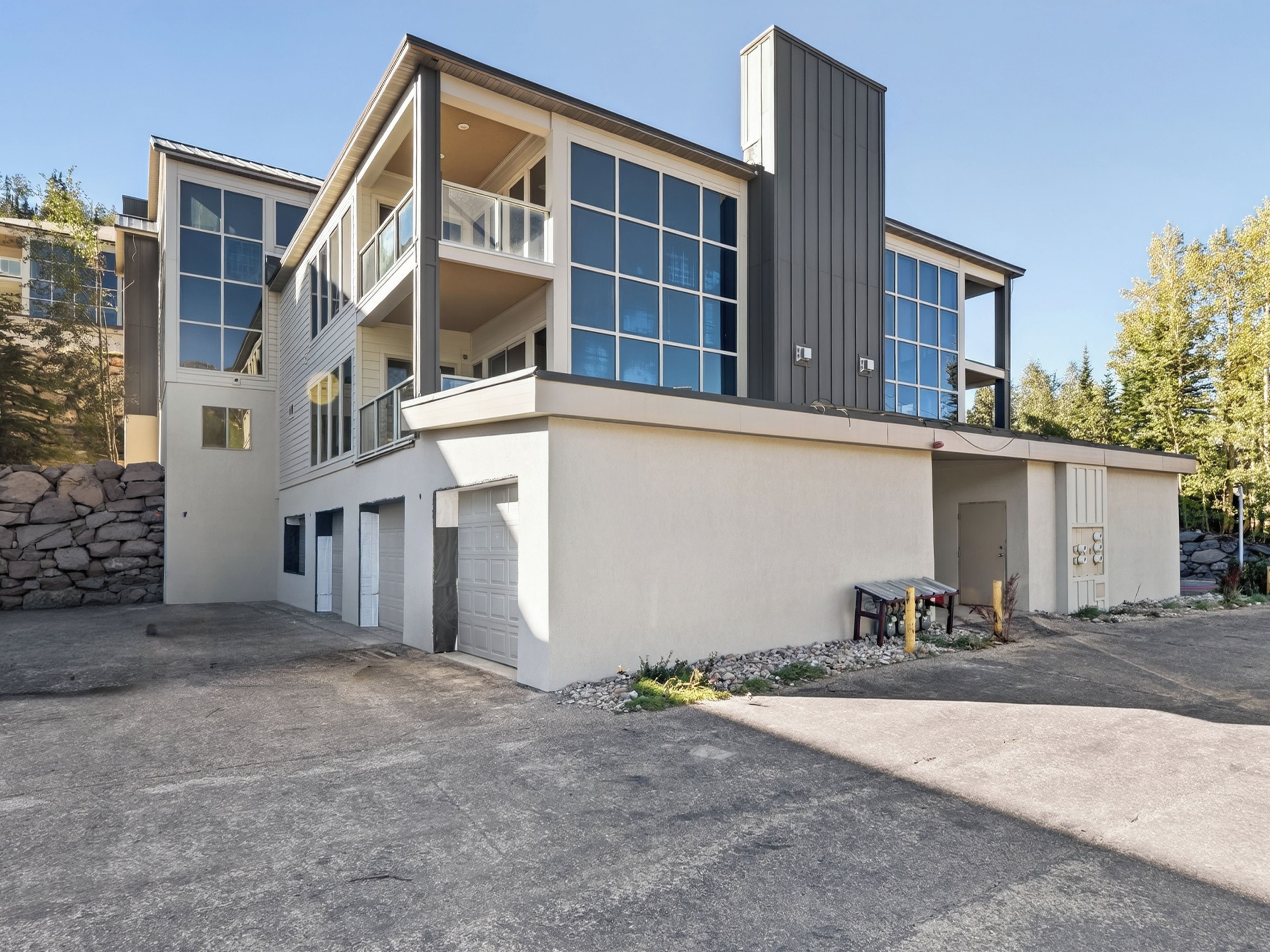 A modern two-story house with a garage, a balcony, and a stone wall.