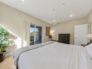 Ein Schlafzimmer mit einem Bett, einem Schminktisch, einer Bank, einer Topfpflanze und einer Schiebetür zu einem Außenbereich.