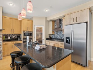 A modern kitchen with wooden cabinets, stainless steel appliances, a large island with bar stools, and pendant lighting. - Magic Carpet 2 bdrm 2 bth plus game loft walking distance to Giant Steps Lifts (Brian Head)