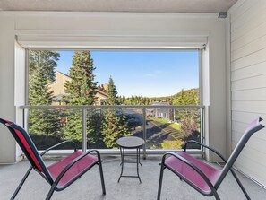 A balcony with two chairs and a small table, overlooking a residential area with houses and trees.