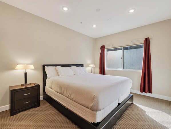 A hotel room with a bed, bedside tables, a window with curtains, and a carpeted floor.