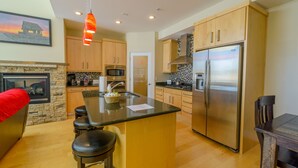 A modern kitchen with a central island, stainless steel appliances, wooden cabinets, and a stone fireplace.