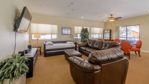 A spacious living room with a large brown leather sofa, a bed, a desk, and a television mounted on the wall.