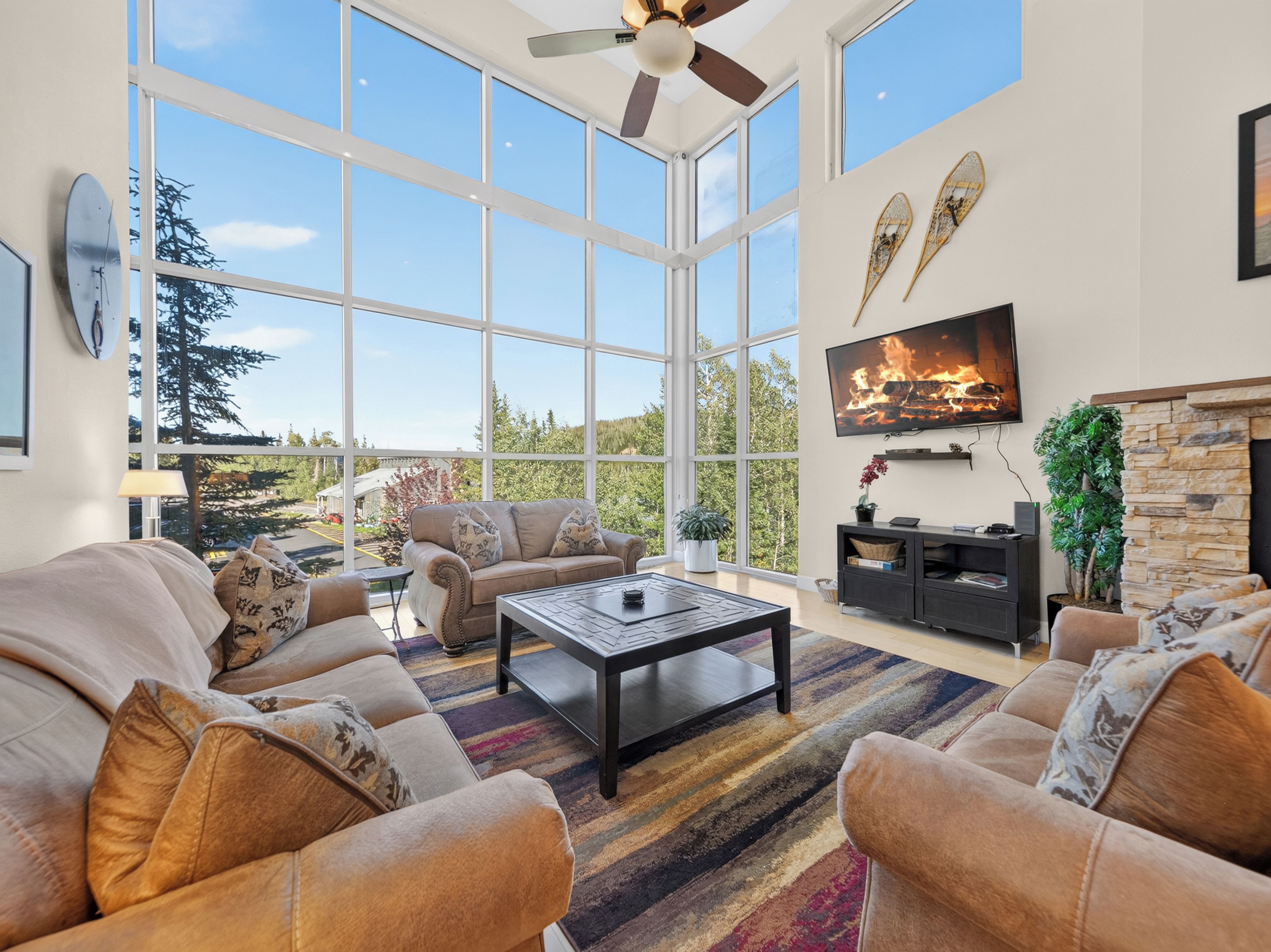 A spacious living room with large windows, a fireplace, and a ceiling fan.