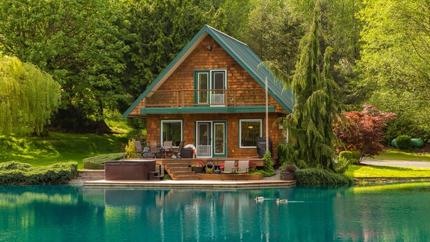 Una casa de madera con balcón, piscina y abundante vegetación.