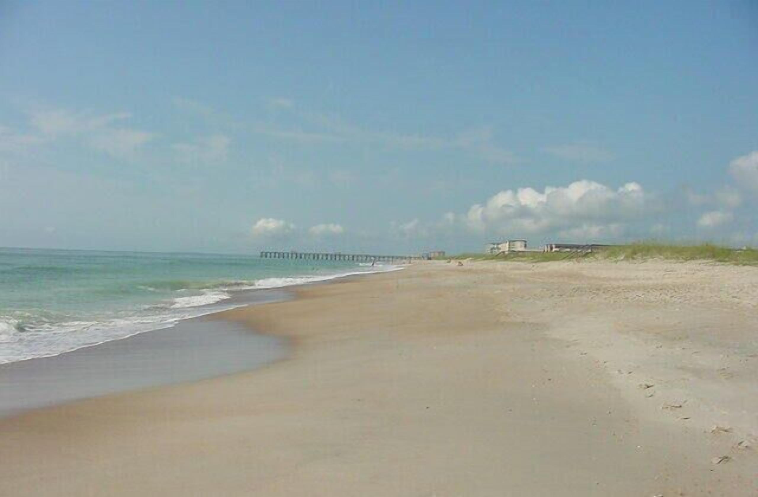 Une plage avec une jetée qui s’avance dans l’eau, un ciel dégagé et des empreintes de pas sur le sable.