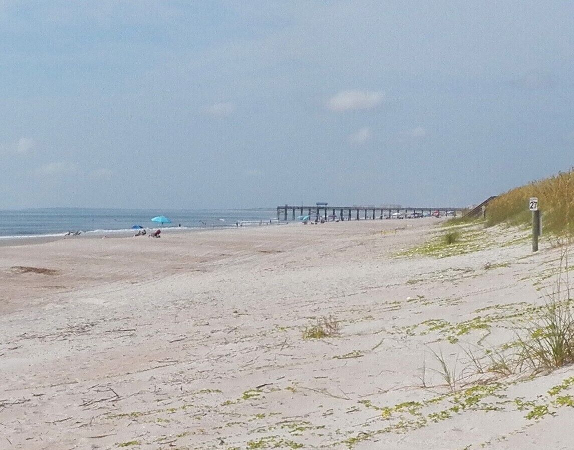 Una playa con un muelle que se adentra en el agua, un cielo despejado y un cartel con el número 27.
