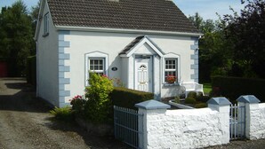 A small, single-story house with a white exterior and a dark tiled roof.