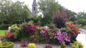 A church with a steeple, surrounded by a well-maintained garden with various flowering plants and trimmed hedges.