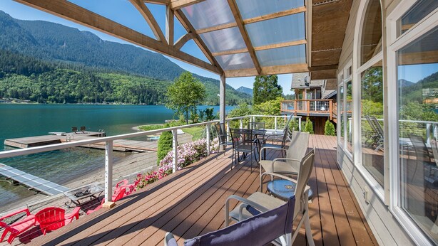 A wooden deck with outdoor furniture overlooking a lake and mountains.