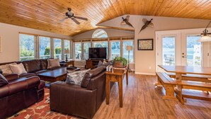A spacious living room with a wooden ceiling, leather sofas, a wooden coffee table, and a large TV.