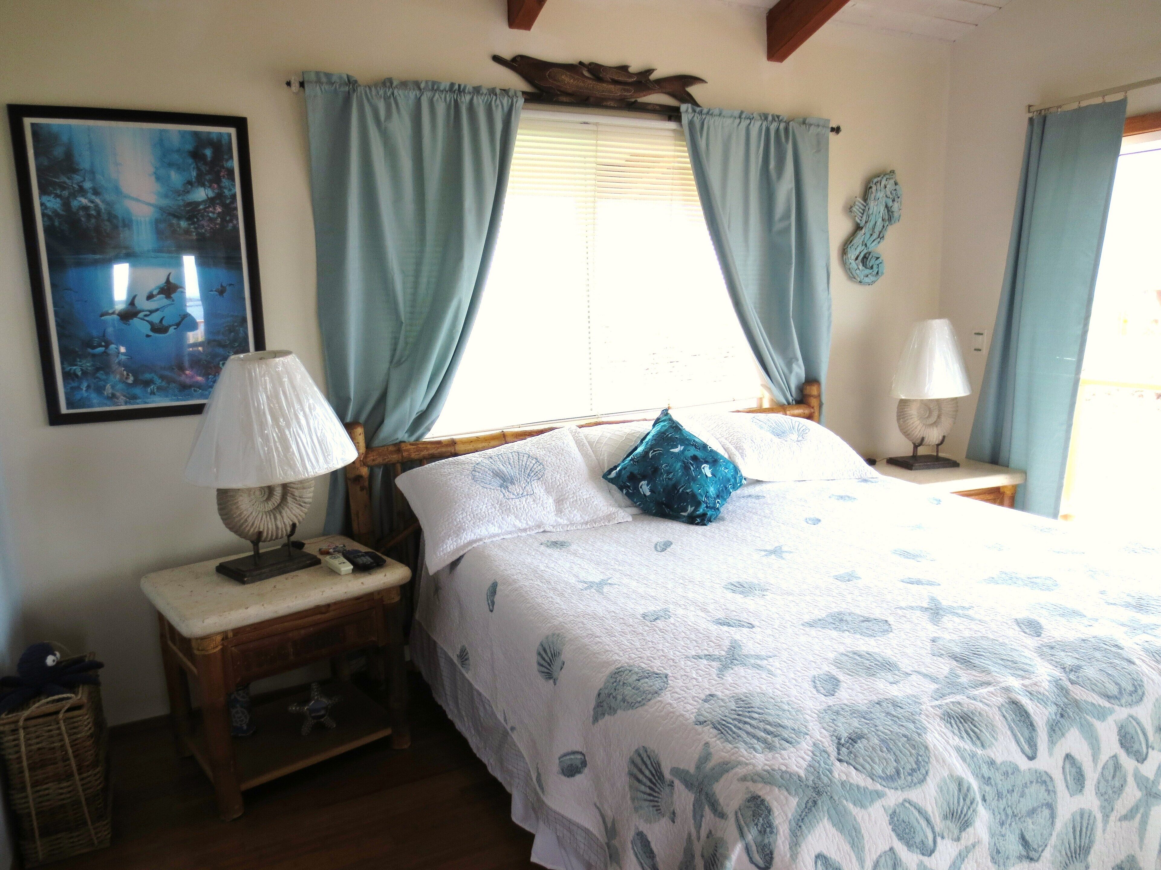 A bedroom with a bed, two nightstands, a lamp, a framed picture, and a window with curtains.