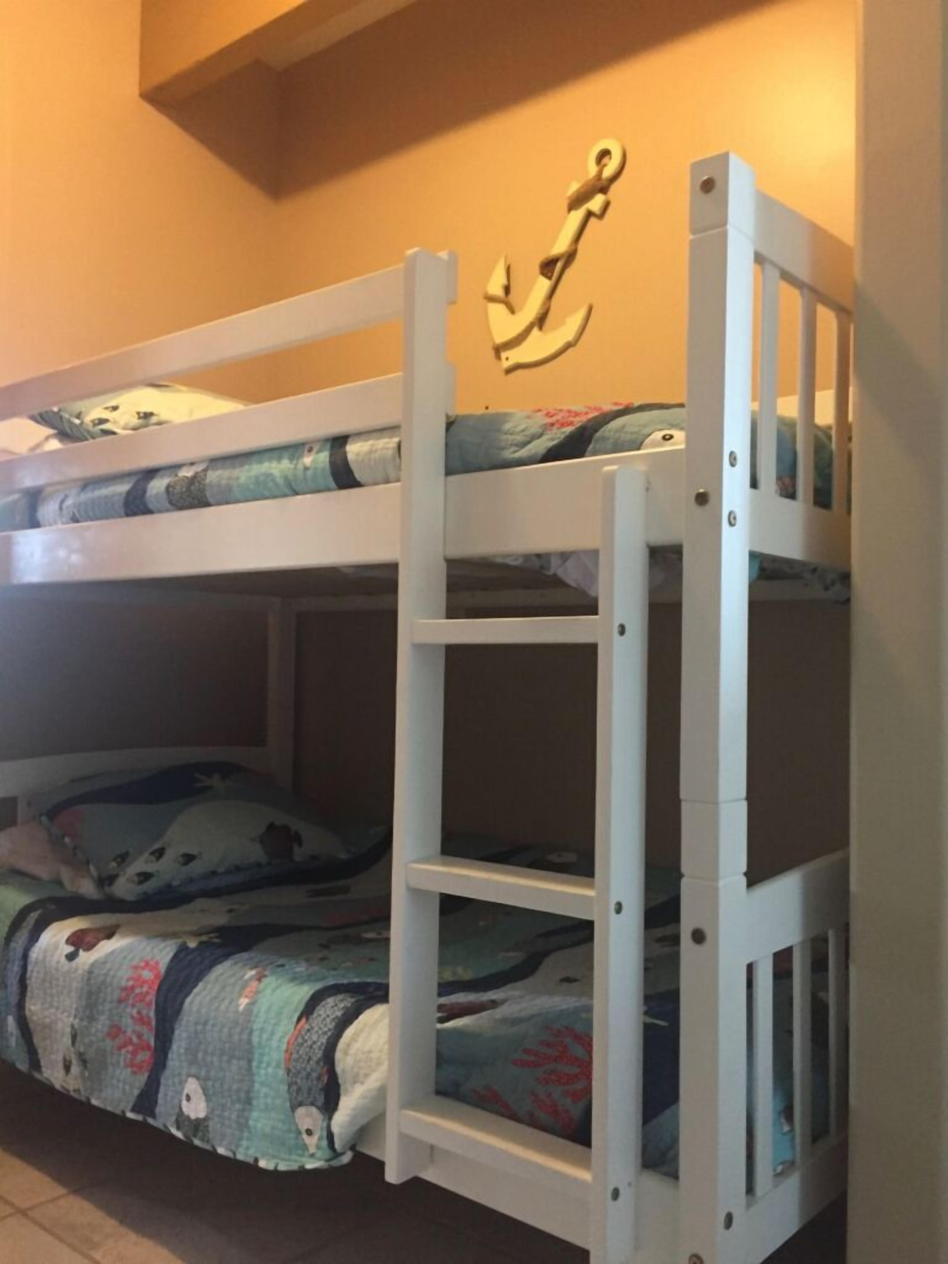 Una cama litera con una escalera, un adorno anclado a la pared y una colcha estampada.