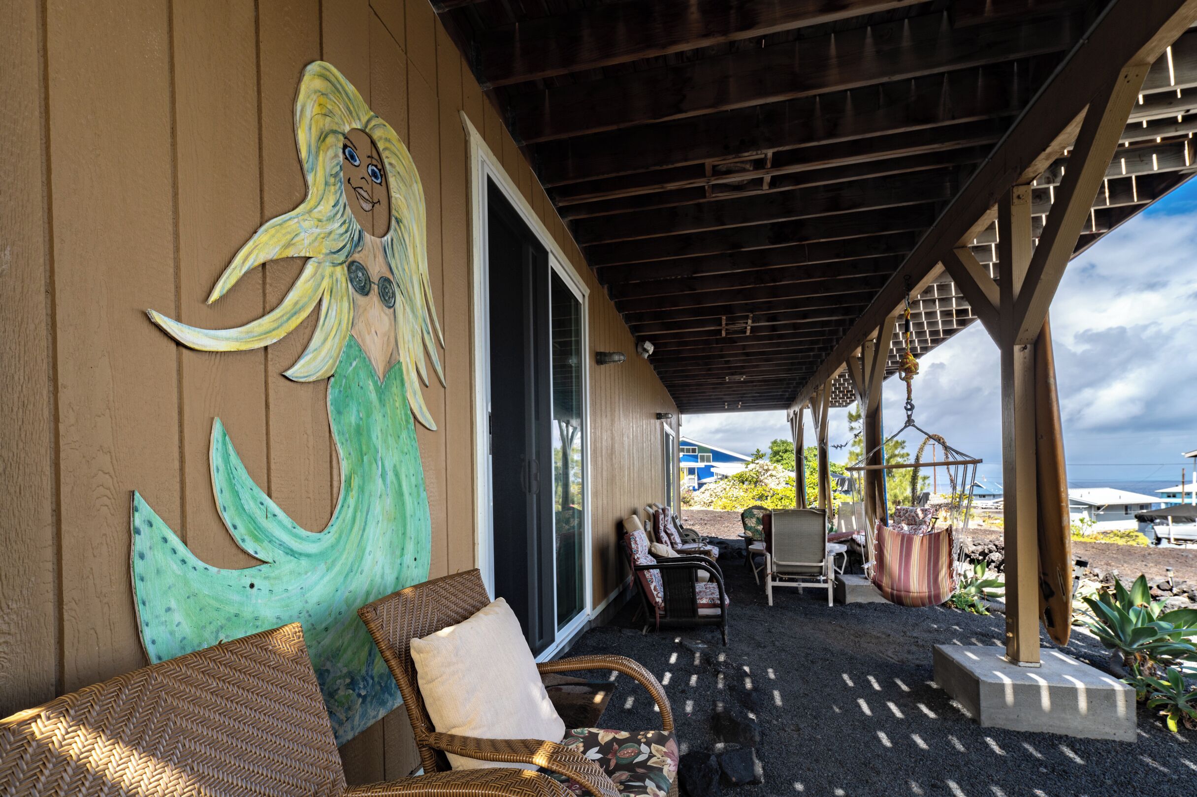 Un espacio de estar al aire libre cubierto con mobiliario de mimbre, un mural y vista al océano.