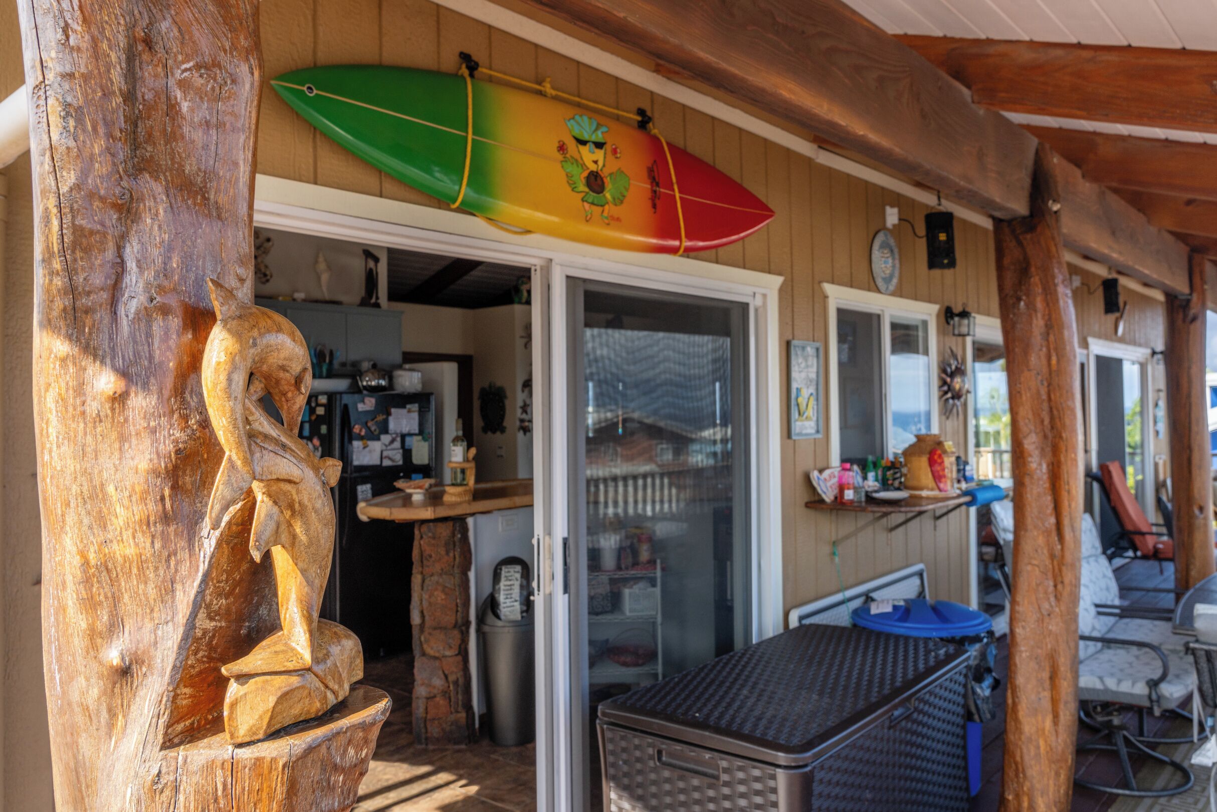 A wooden structure with a surfboard, a statue, and a covered outdoor area with a table and chairs.