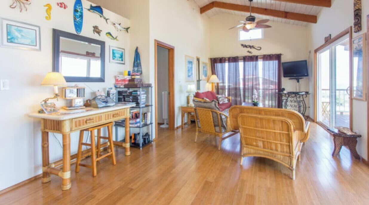 A spacious living area with a wooden floor, a dining table, and a sofa. There are wall decorations including framed pictures and a surfboard.
