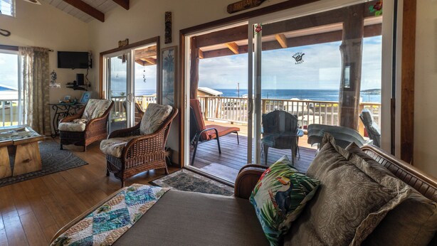 A cozy living room with wicker furniture, a large window with a view of the ocean, and a wooden deck outside.