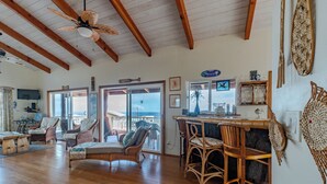 A spacious living room with wooden floors, wicker furniture, a ceiling fan, and a view to the outside.