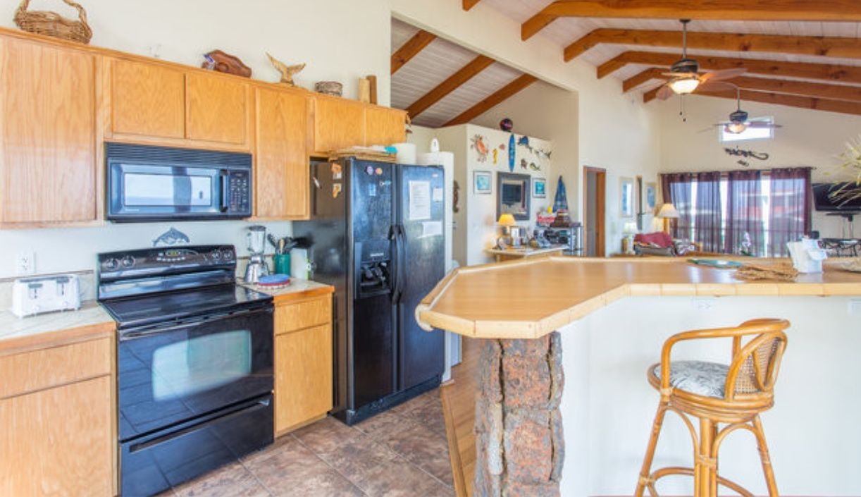 A kitchen with wooden cabinets, a black refrigerator, and a stone island with a chair.