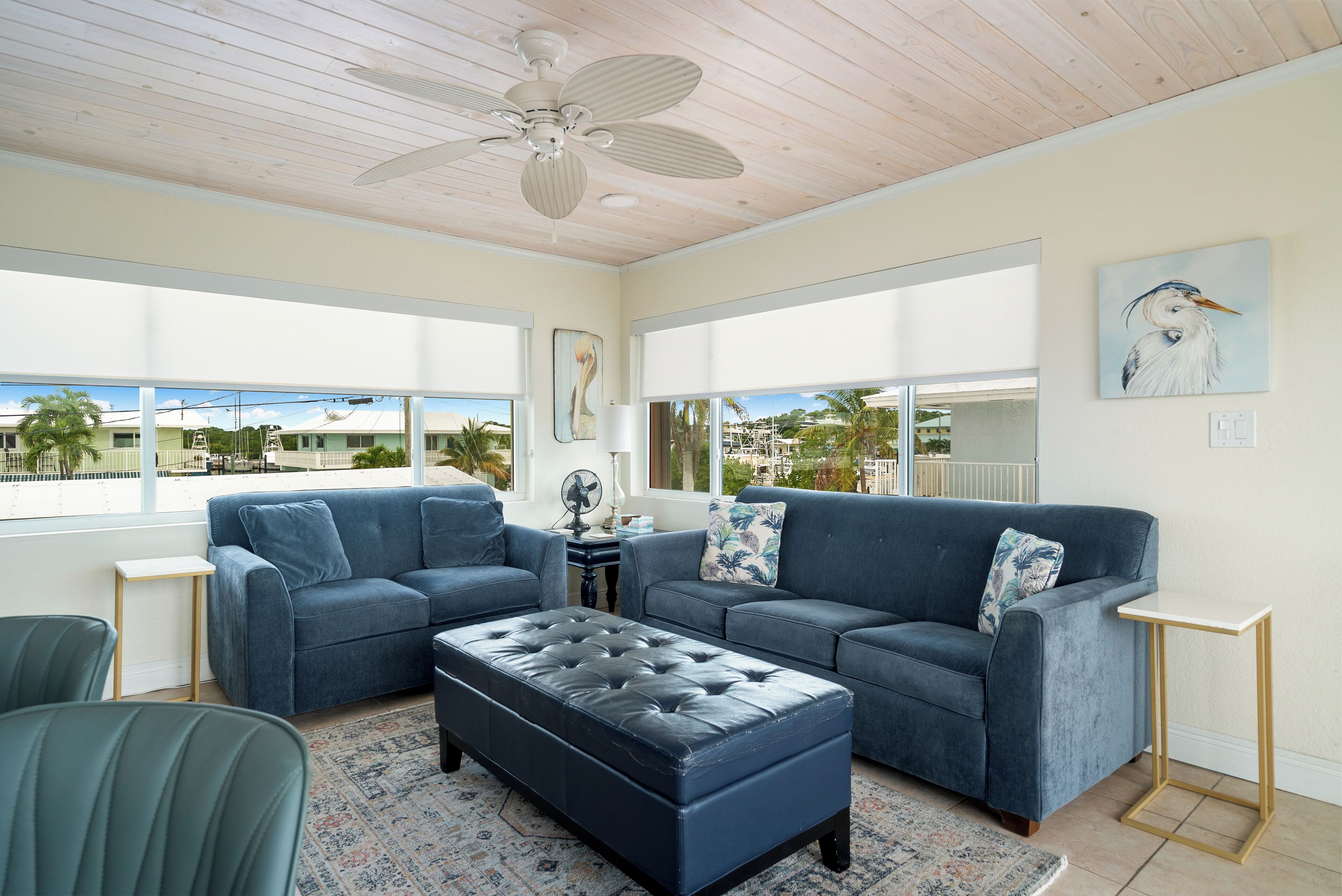 A living room with a blue sofa set, a matching ottoman, and a ceiling fan.