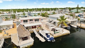 A marina with multiple boats docked, a thatched-roof structure, and several buildings with balconies and outdoor seating areas. - Nov 18-Jan 1 Open... Live Like a Local*Waterview*Pet Friendly*Key Largo MM 99.5*Manatees (Key Largo)