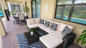 Un patio couvert aménagé avec un canapé d’angle, une table basse et une table à manger avec des chaises. On peut apercevoir une piscine à travers les portes vitrées.
