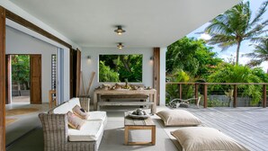 Un vaste espace de vie extérieur comprenant un canapé, une table basse et des coussins, avec vue sur un jardin luxuriant et des palmiers.