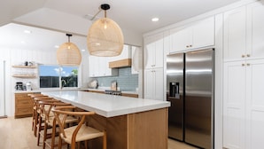 Une cuisine moderne dotée d’un îlot central, d’appareils électroménagers en acier inoxydable et de luminaires suspendus en osier.