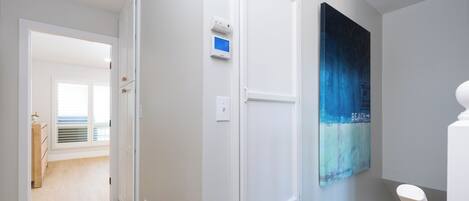 A hallway with a white door, a thermostat, and a wall-mounted artwork depicting a beach scene.