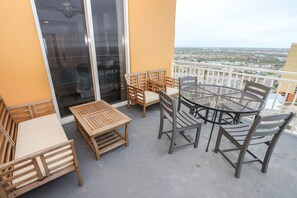 A balcony with wooden furniture, including a sofa, chairs, and a round table. - Splash Penthouse Amazing Panoramic Views! Free Beach Chair Set-Up! (Panama City Beach)