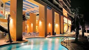 Zona de piscina amb vora corba, palmeres i mobiliari exterior.